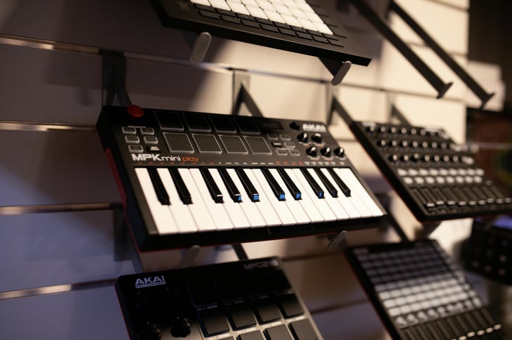 Close-up of an Akai MPK mini play MIDI controller keyboard displayed on a store wall.
