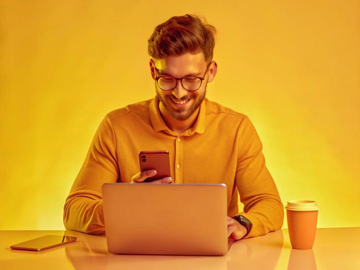 A gaming developer, working on a laptop and 2 mobile devices (one on Apple iOS, one on Android) in a vibrant and creative environment, surrounded by colorful digital assets. The lighting is bright and cheerful, highlighting the creativity involved.